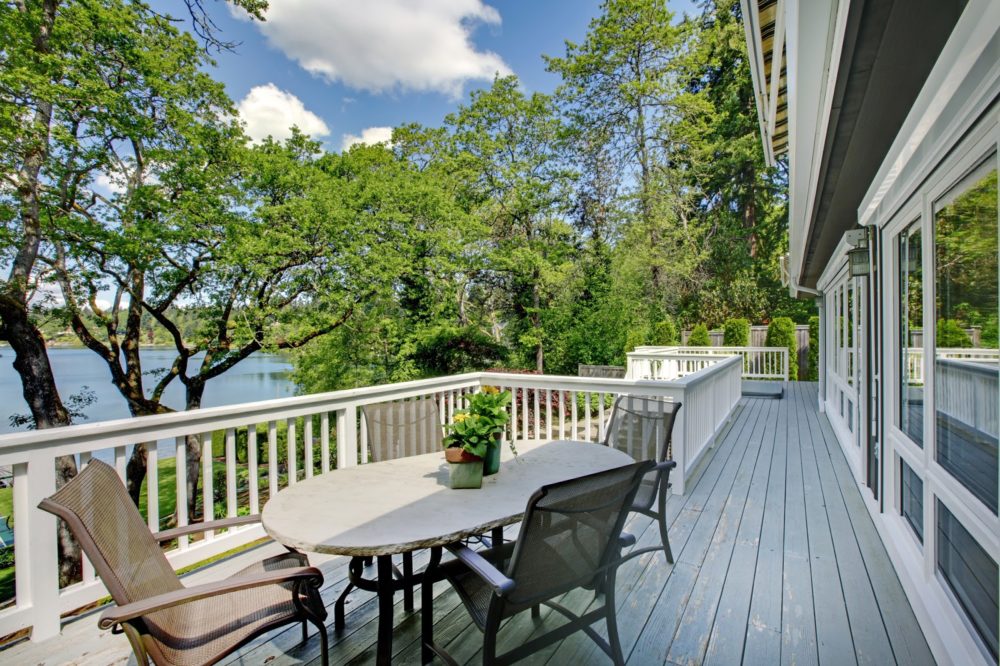 Large long balcony home exterior with table and chairs, lake view.